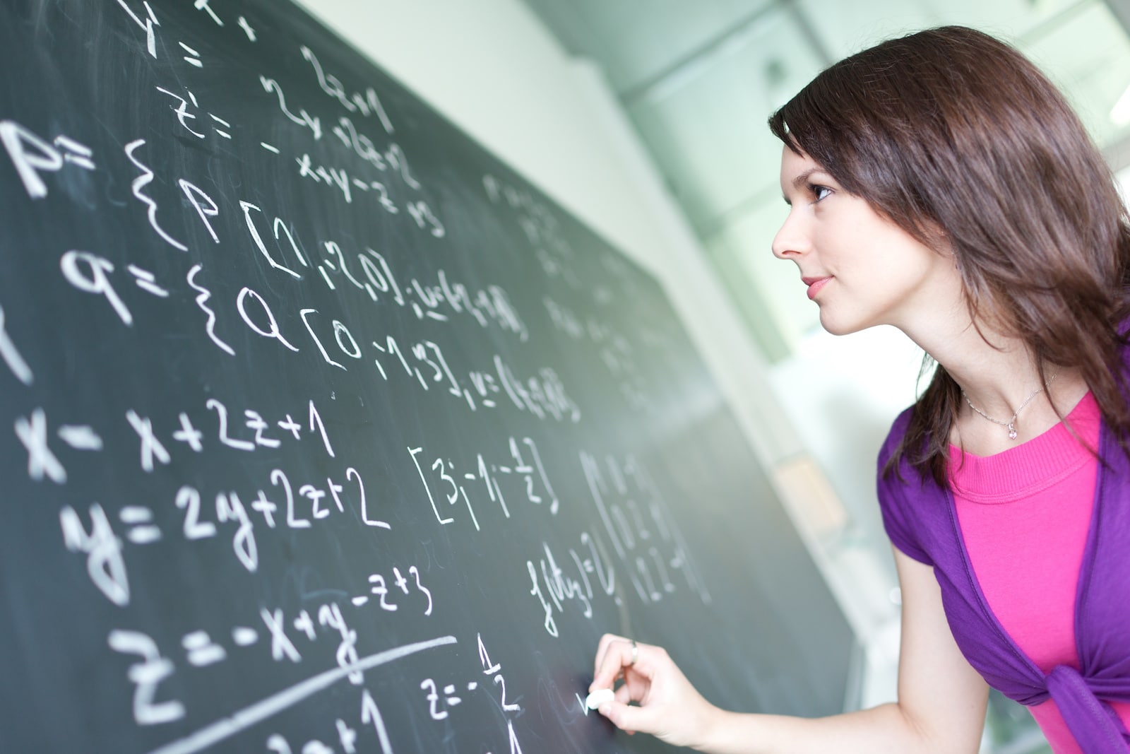 pretty young college student writing on the chalkboard/blackboard during a math class