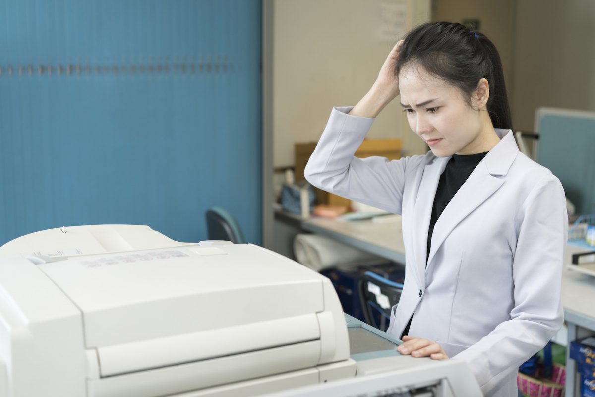 stress young asian businesswoman looking at paper stuck in printer at office